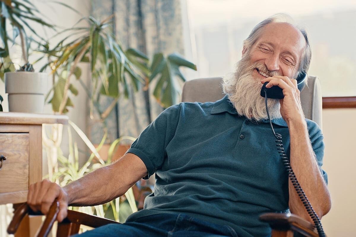 Senior man laughing on a corded phone in his armchair at home during a reminder call