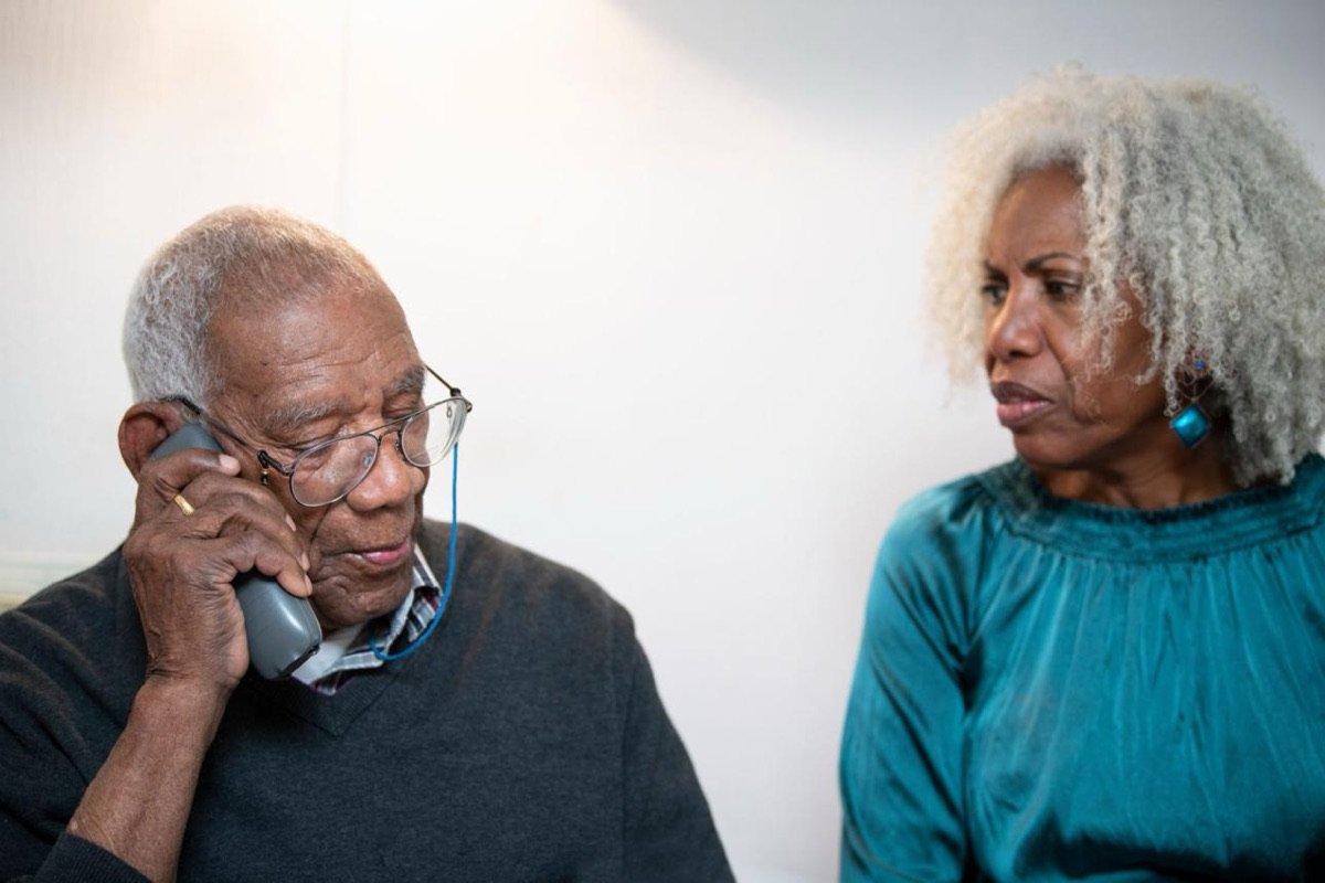 Elderly father taking a medication reminder call while his wife listens beside him