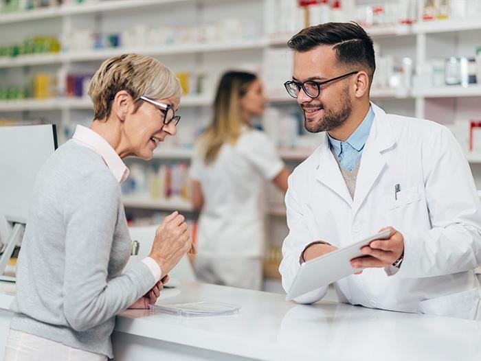 Pharmacist at the counter talking with an older customer about her medication schedule
